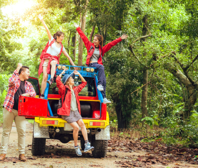 Happy asian young travellers with 4WD drive car off road in forest, young couple looking for directions on the map and another two are enjoying on 4WD drive car. Young mixed race Asian woman and man.