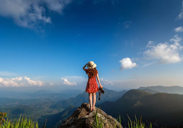 Woman hand holding camera and standing on top of the rock in nat