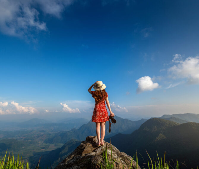 Woman hand holding camera and standing on top of the rock in nature. Travel concept.